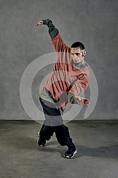 Stately fellow with tattooed face, beard. Dressed in colorful jumper, black pants and sneakers. Dancing, gray background