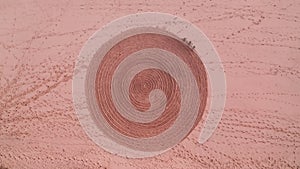 Static aerial top view of people trampling down mysterious spiral circus on sand. Fake mystery and sports exercise for