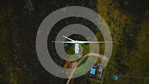 Static top view drone shot, windmill turbine spinning in the middle of green forest, alternative energy source concept.