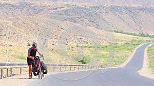 Static view caucasian male cycle solo push red bicycle uphill on asphalt in extreme heat outdoors in scenic mountains