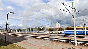 The station has laid tracks, tiled passing platforms, and power lines stretched out on concrete poles. A train of passenger railwa