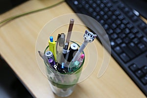 Stationary glass that contain a lot of pens and pencils.