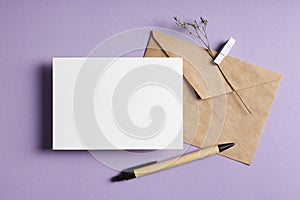 Stationary greeting card mockup with envelope, pen and dry flower twig on lavender color background