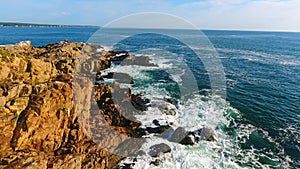 Stationary view of Cliffs of ocean in Maine with waves crashing over boulders