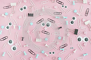 Stationery buttons, paperclips and asterisks in disorder on a pale pink background.Funny faces with puppet eyes and
