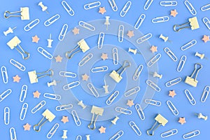 Stationery chaotically scattered on a blue background. White paper clips, clerical buttons and small pink stars in the