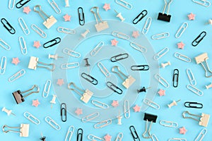 Stationery chaotically scattered on a turquoise background. White and black paper clips, clerical buttons and small pink