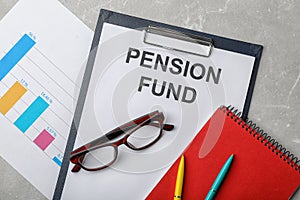 Stationery, glasses, notebook, chart and paper with words PENSION FUND on table