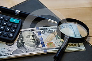 Stationery items:dollar, pen, calculator, magnifier and notepad on a wooden table...