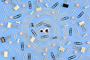 Stationery and puppet eyes are chaotically scattered on a blue background. In the center there is a smiley face made of