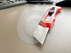 Stationery on the table in the office. stationery knife with a red, plastic handle. paper cutting, tool for work. knife with a