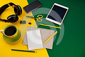 Stationery on the table top view. Yellow and green bright background. Notepad for notes with place for text. Work at home. A cup