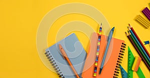 Stationery is on a yellow background. Top view of notepads, pens and colored pencils on a yellow background.