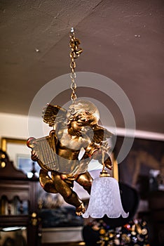 Statue of angel. Gold angel. A flower arrangement hanging from ceiling with lamp wooden background. On chain old vintage house