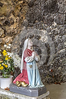 Statue of Bernadette praying to Our Lady of Lourdes with flowers next to her