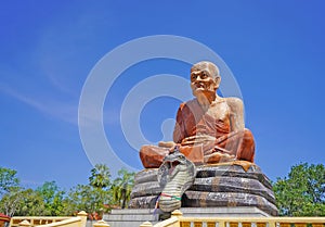 A statue of the Buddha  in Thailand  who sits against the blue sky  a large snake near his feet.