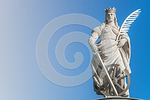 Statue of Catherin with writing bird feather, sword and cartwheel at ancient portal in Magdeburg, Germany, closeup, gradient blue