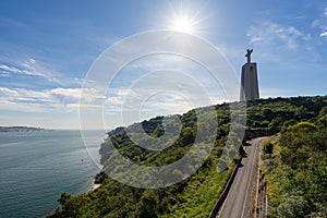 statue of Christ in Almada/Lisbon, with the morning sun falling on the tarred road and the Tagus River