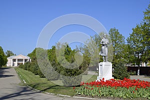 Statue of a collective farmer on a pedestal. The legacy of the Soviet era. A flower bed with tulips and young trees in