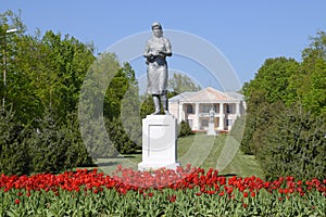 Statue of a collective farmer on a pedestal. The legacy of the Soviet era. A flower bed with tulips and young trees in