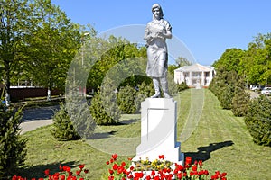 Statue of a collective farmer on a pedestal. The legacy of the Soviet era. A flower bed with tulips and young trees in