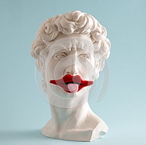 Statue of  David  head  with  with red lips and protruding tongue on  blue background. Minimal art poster