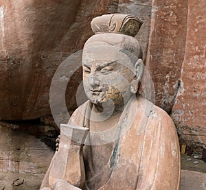 Statue of disciple or follower holding bottle in front of giant Buddha at Dazu Rock Carvings