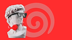 Statue. Earphone on a red background. Gypsum statue of David`s head. Creative. Plaster statue of David`s head .