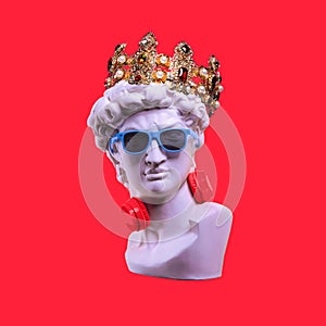 Statue. Earphone on a red background. Gypsum statue of David`s head. Creative. Plaster statue of David`s head in blue sunglasses