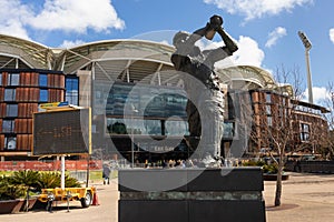 Statue of a football player in front of the Adelaide Oval. People entering the stadium before an Australian football match. Team