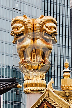 Statue of a golden lion on the roof of a Buddhist temple against the backdrop of a modern building