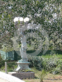 Statue of a greek goddess who carries a five-pointed lamp wreath at a street in St. George - Agios Georgios Corfu, Greece