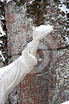 A statue hand full of snow with natural rock as background