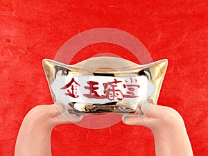 statue hands holding antique chinese gold ingot money isolated on red paper background