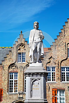 Statue of Hans Memling and medieval house exterior against blue sky in Brugge, Belguim