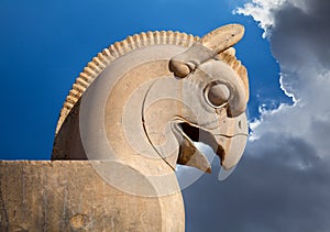 Statue of Huma or Homa Bird as decorative Column head in Persepolis against Blue Sky with White Clouds