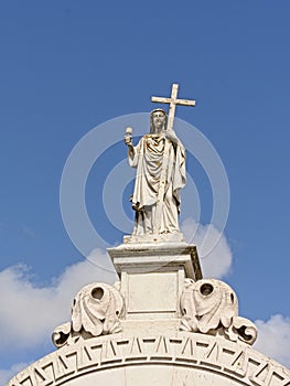 Statue of Jesus christ holding a cross on top of a grave tomb in Altode Sao Joao cemetery, Lisbon