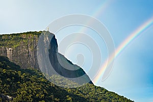 Statue of Jesus Christ on top of a cliff with the rainbow in the blue sky in Rio de Janeiro