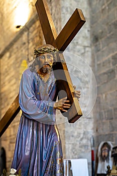 Statue of Jesus holding a wooden cross. The statue is made of wood in a holy week procession