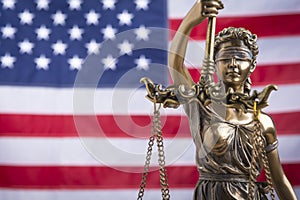 The statue of justice Themis or Iustitia, the blindfolded goddess of justice against a flag of the United States of America