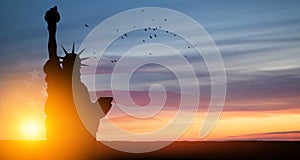 Statue of Liberty with american flag on background of sunset sky.