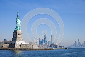 Statue of Liberty in NY Harbor on bright sunny day with blue sky and Manhattan in the distance
