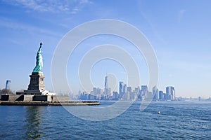 Statue of Liberty in NY Harbor on bright sunny day with blue sky and Manhattan in the distance