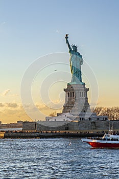Statue of liberty vertical with red boat during sunset in New York City, NY