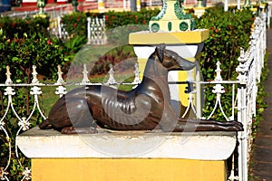 A statue of a lying dog on a pedestal. Plaza Mayor. Trinidad city, Cuba