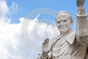 Statue of pope John Paul II blessing people, with cloudy sky in