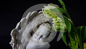 Statue of sad angel with tulip flowers as symbol of pain, fear and end of life. Remembrance concept