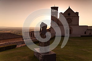 The statue of St. Francis with the Basilica of Assisi in the background at sunset