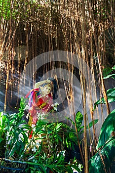 Statue by a stream in the mist among tropical plants, orchids and lianas, in the park of wat saket, or the golden mount temple.