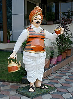 Statue of a tea vendor in a colourful garb and turban with a tea kettle and raising a tea cup